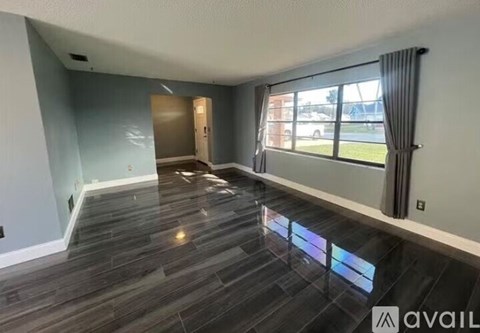 A spacious room with a grey floor and a large window with curtains.