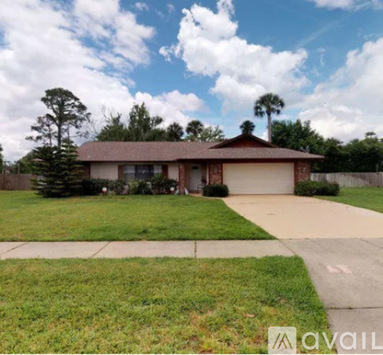 A house with a brown roof and a white garage door is surrounded by a green lawn and trees.