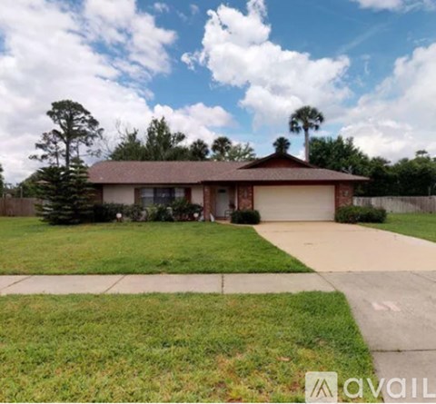A house with a brown roof and a white garage door is surrounded by a green lawn and trees.
