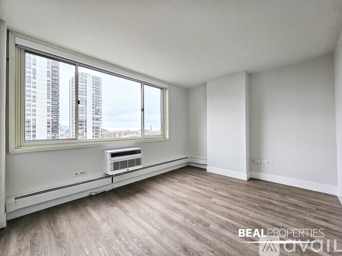 A room with a window overlooking a cityscape and a small air conditioning unit on the window sill.