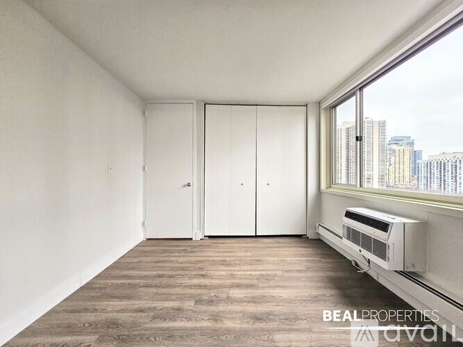 A room with a window, a wall-mounted air conditioner, and a wooden floor.