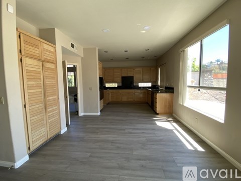 A spacious living room with wooden flooring and a kitchen area in the background.