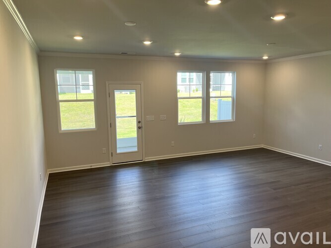 A spacious room with wooden flooring and two windows.