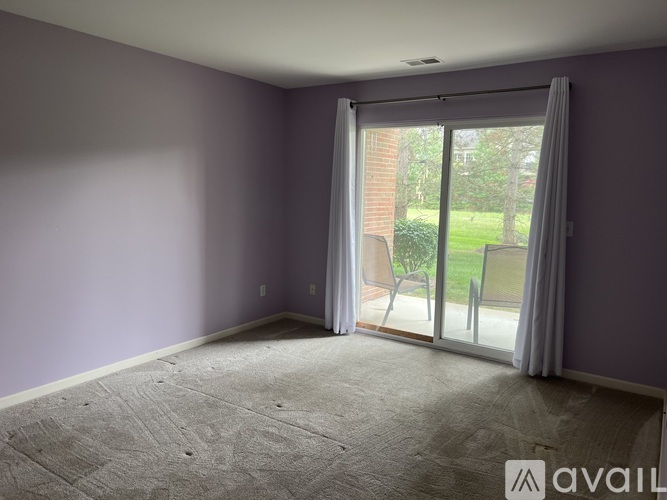 A room with purple walls and a carpeted floor with a sliding glass door leading to a patio.
