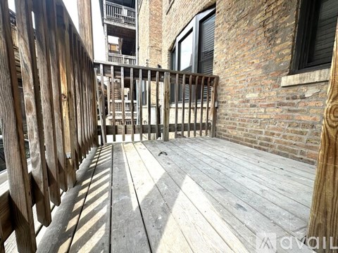 A wooden deck with a railing and a brick building in the background.