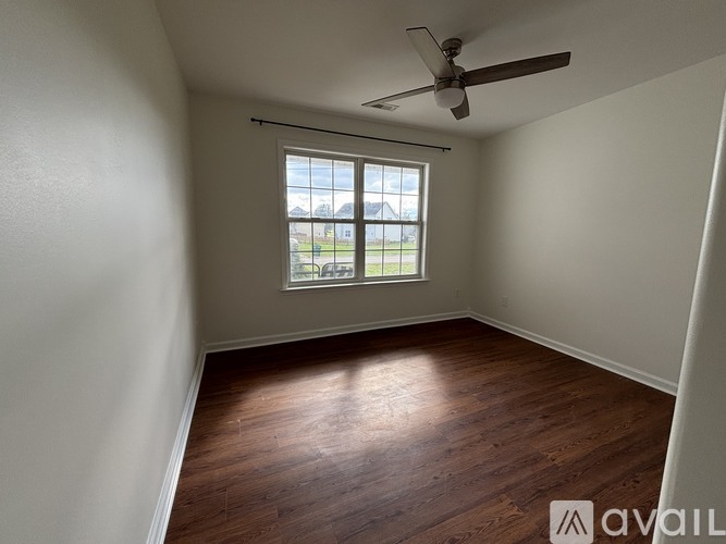 A room with a ceiling fan and a window overlooking a green area.