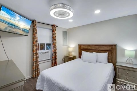 A bedroom with a large bed, a flat-screen TV mounted on the wall, and a ceiling fan.