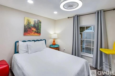 A bedroom with a bed, a painting on the wall, a window with curtains, and a yellow chair.