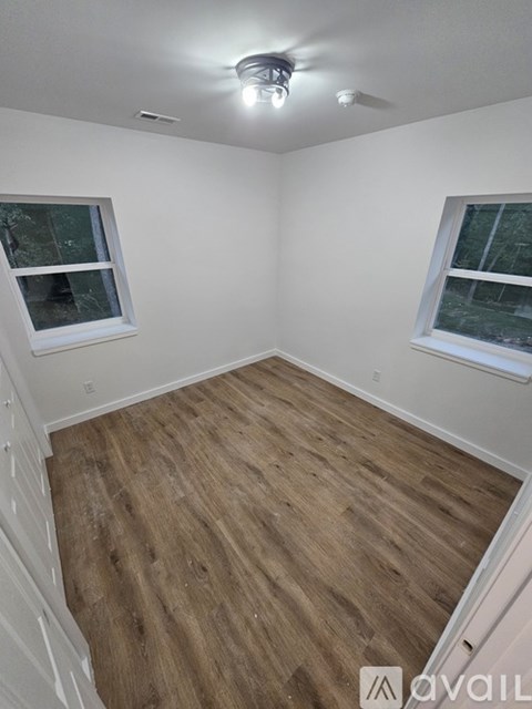 A room with wooden flooring and two windows.