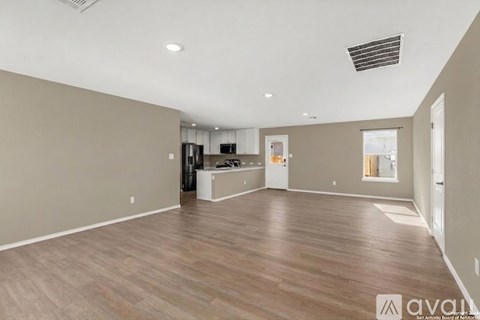 A spacious living room with wooden flooring and a kitchen area in the background.