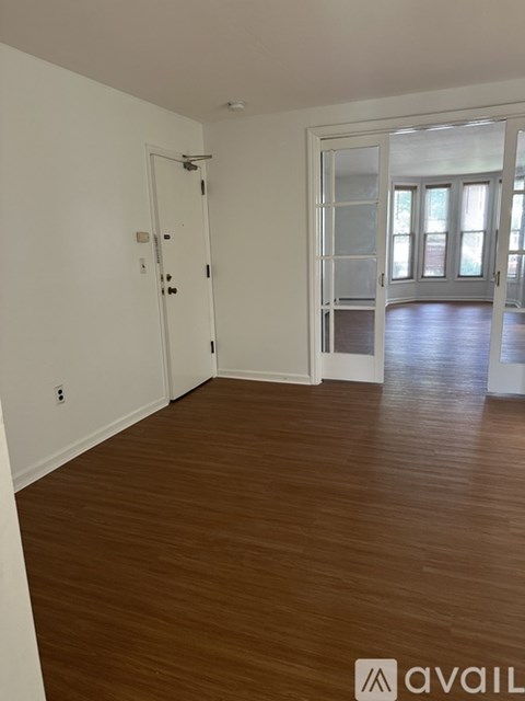 A room with a white door and a window with a view of trees.