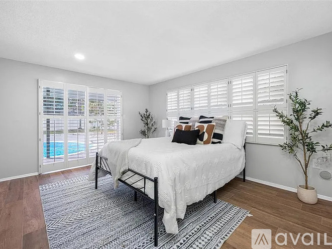 A bedroom with a large bed and a view of a pool through the window.