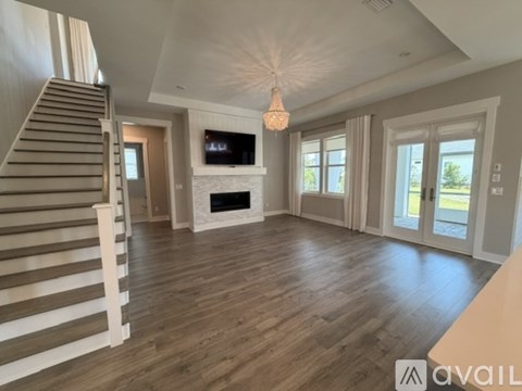 A spacious living room with a staircase on the left and a television mounted on the wall.