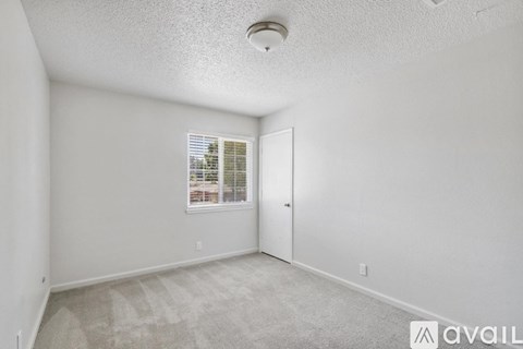 A room with a carpeted floor, a window with blinds, and a door.
