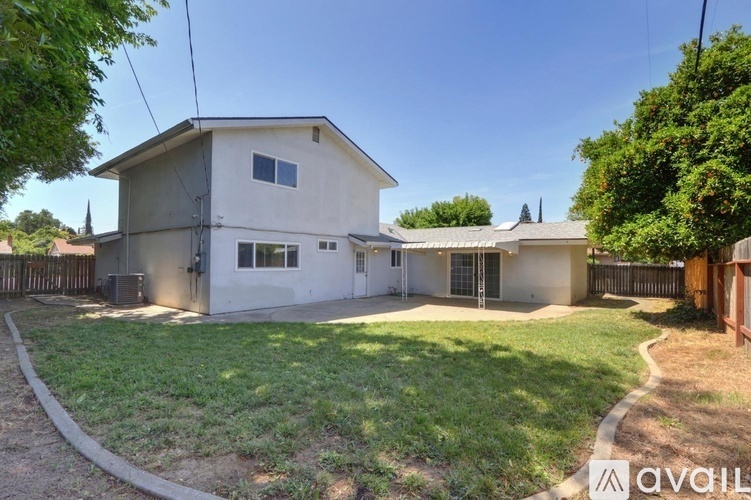 A house with a white exterior and a grey roof is surrounded by a fence and has a green lawn.