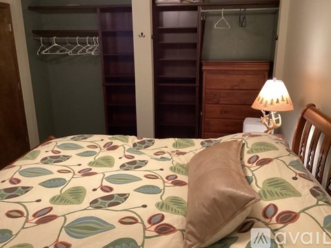 A bed with a leaf patterned comforter and a brown pillow is in a room with a wooden wardrobe and a lamp.
