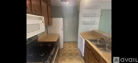 A kitchen with a black stove top oven, white microwave, white refrigerator, and a wooden counter top.