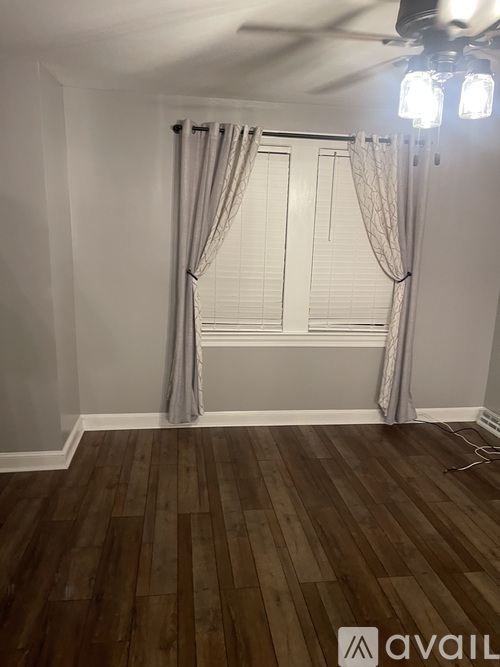 A room with wooden flooring and a window with curtains.