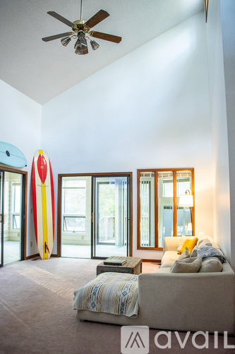 A living room with a couch and a surfboard leaning against the wall.