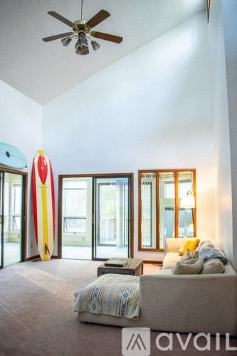 A living room with a couch and a surfboard leaning against the wall.