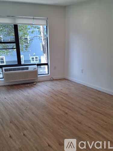 A room with wooden flooring and a window with a view of a building outside.