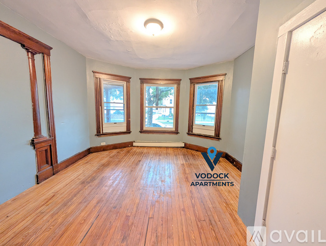 A spacious room with wooden floors and three windows.