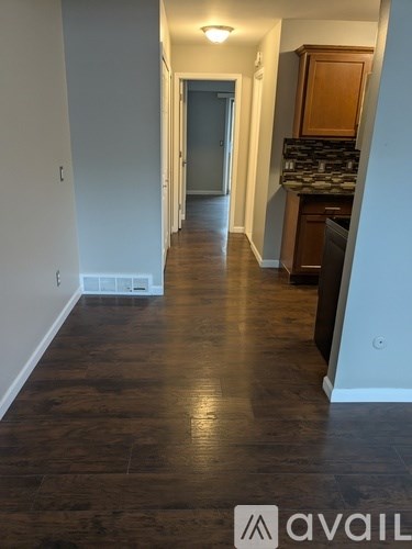 A hallway with wood floors and a kitchen area in the distance.