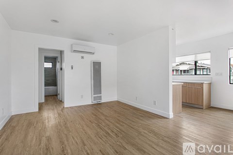 A spacious room with wooden flooring and a white wall with a window.