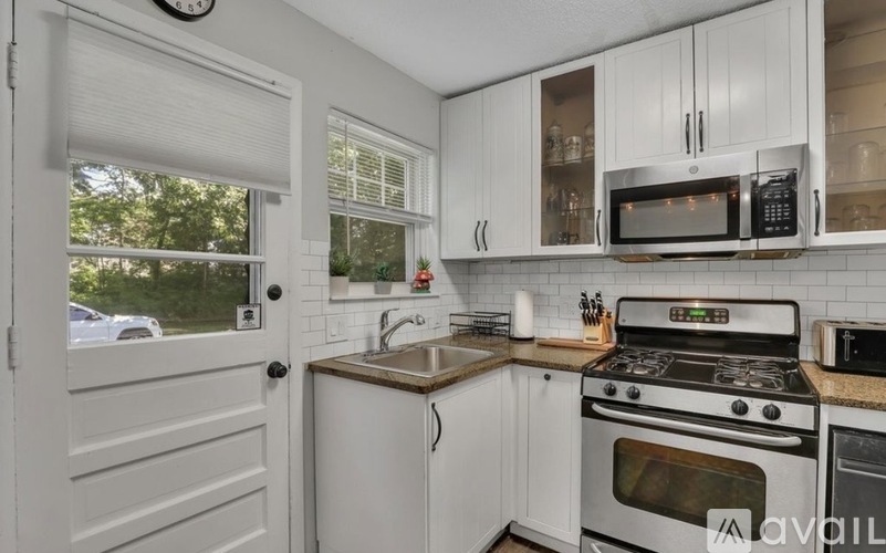 A kitchen with white cabinets and appliances, a sink, and a window with blinds.