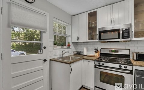 A kitchen with white cabinets and appliances, a sink, and a window with blinds.