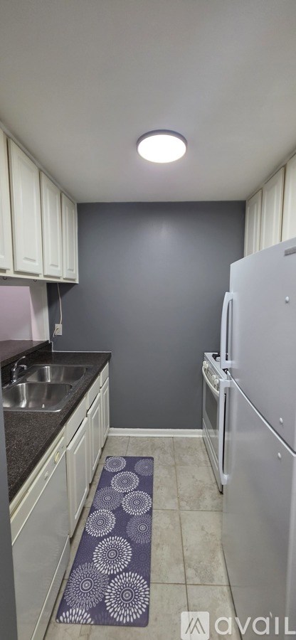 A kitchen with a white refrigerator and a purple mat on the floor.