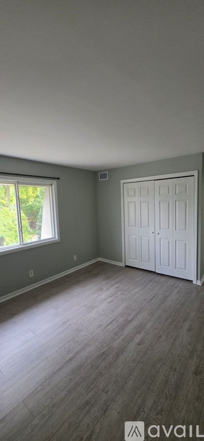 A room with a white door and a window with a view of trees outside.