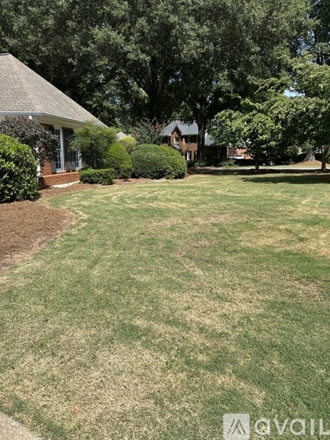 A well-maintained lawn with a house and trees in the background.