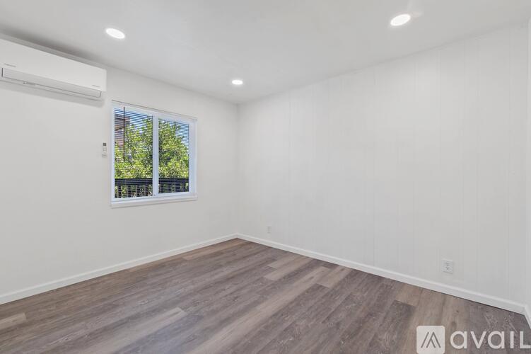 A room with wooden flooring and a window showing trees outside.