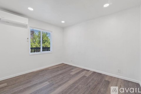 A room with wooden flooring and a window showing trees outside.