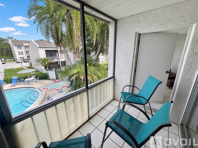 A balcony with two chairs and a view of a pool and houses.
