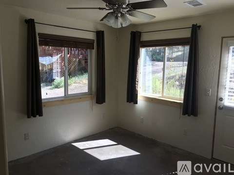 A room with a ceiling fan and two windows with curtains.