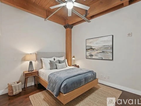A bedroom with a bed, a ceiling fan, and a painting on the wall.