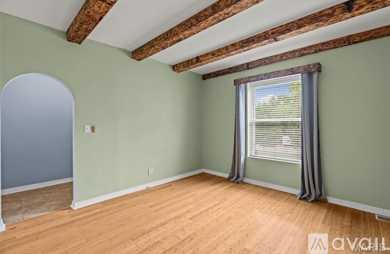 A room with wooden beams on the ceiling and a window with curtains.