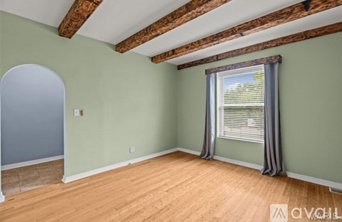 A room with wooden beams on the ceiling and a window with curtains.