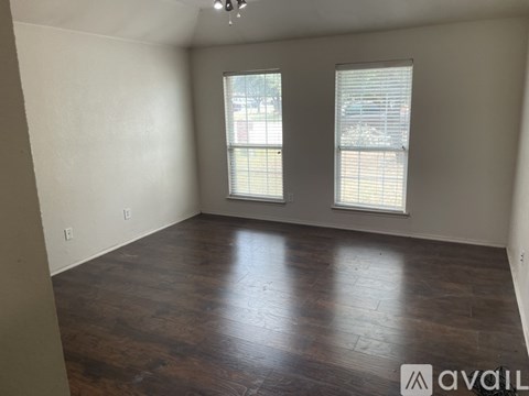A room with wooden flooring and two windows.