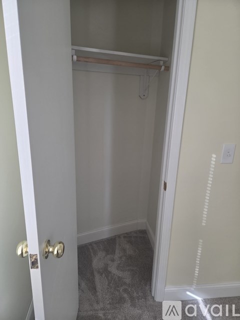 A white door with a gold handle is open to a small, empty room with a carpeted floor.