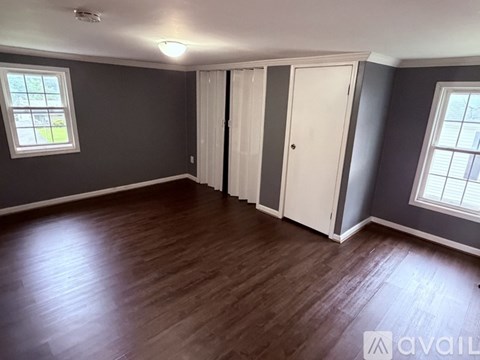 A room with wooden flooring and two windows.