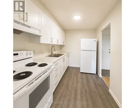 A white kitchen with a stove top oven, sink, and refrigerator.