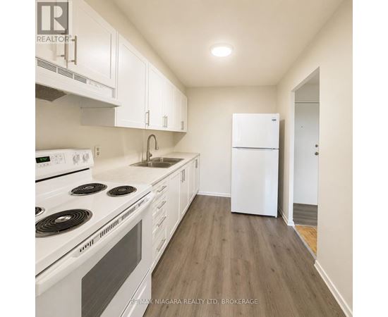 A white kitchen with a stove top oven, sink, and refrigerator.