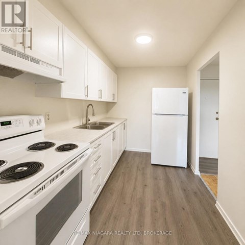 A white kitchen with a stove top oven, sink, and refrigerator.