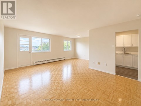 A spacious room with wooden flooring and white walls.