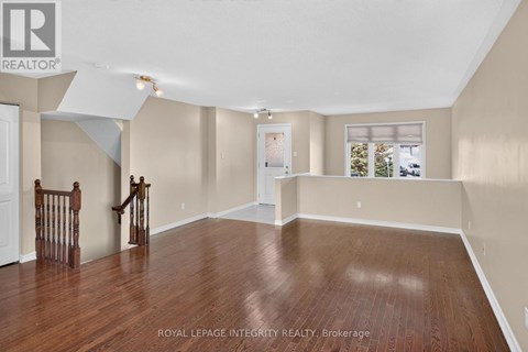 A spacious room with wooden flooring and a staircase with a wooden railing.