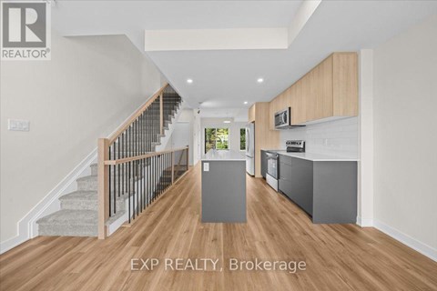 A spacious room with wooden floors and a staircase with a metal railing.