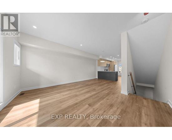 A room with wooden flooring and white walls, with a brokerage logo on the top left.